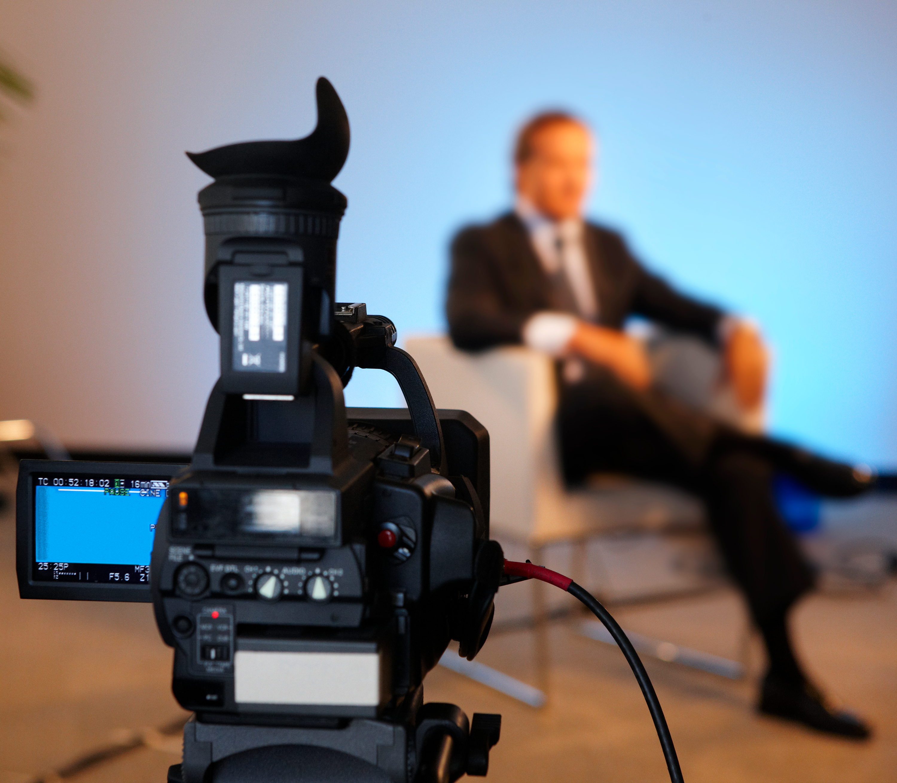 A person sitting in a chair as they are being recorded by a camera in a professional environment.