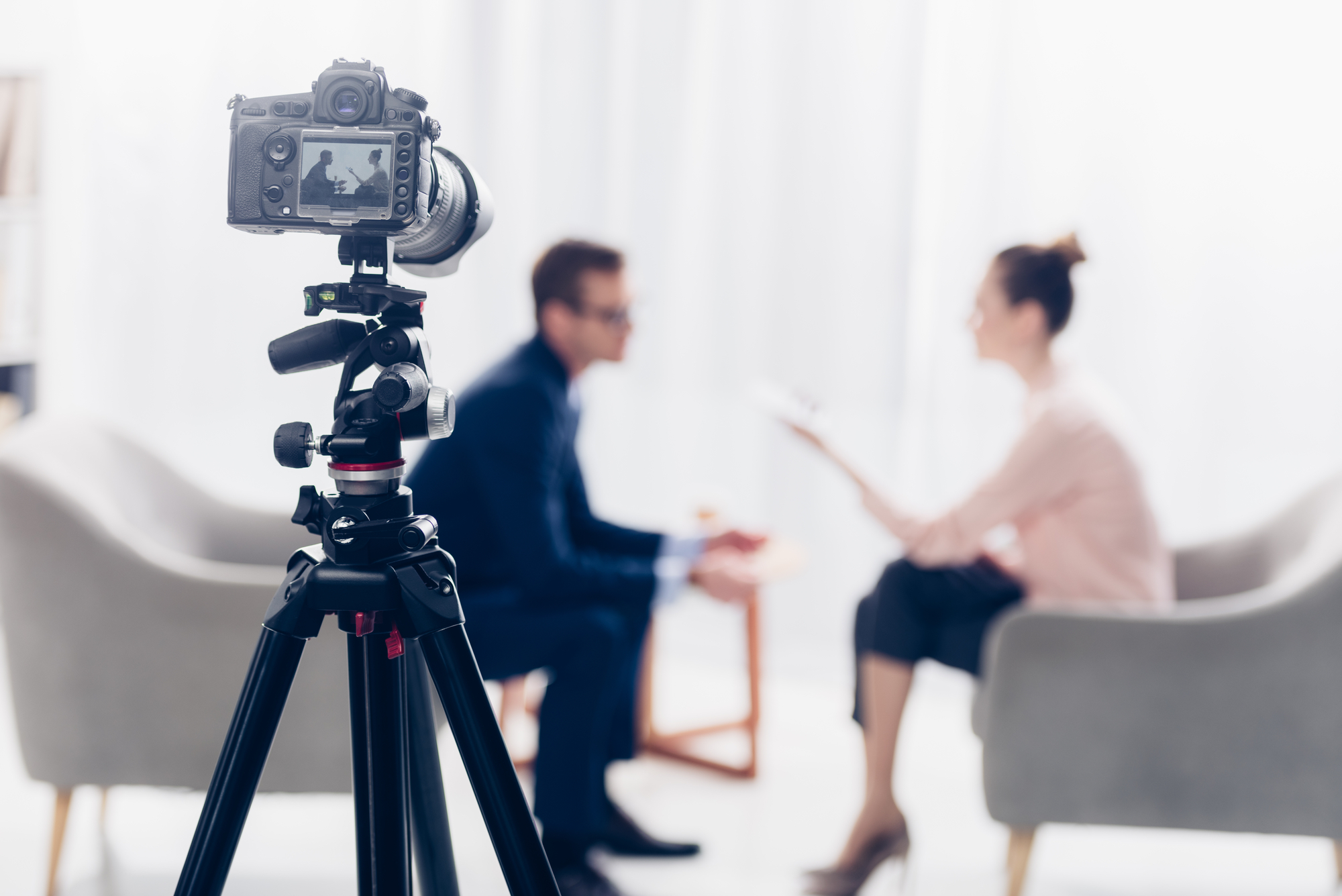 A video camera recording two people discussing a legal case in two chairs across from each other.